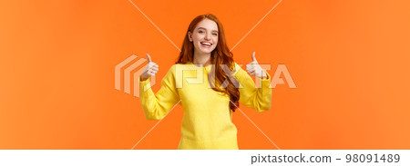 Holidays, gestures, people concept. Cheerful cute redhead girl smiling and showing thumbs-up recommend product, give positive reply, agree or like something, nod agreement, orange background 98091489