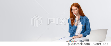 Serious looking focused and determined redhead female working over important project, design for company, work freelance, thinking, pondering as writing, stand near laptop and colored pencils Serious looking focused and determined redhead female working over important project, design for company, work freelance, thinking, pondering as writing, stand near laptop and colored pencils 98091665