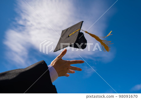 Close-up of a woman's hand with a graduation cap against the blue sky. Close-up of a woman's hand with a graduation cap against the blue sky. 98091670