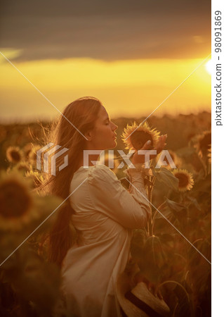 Beautiful middle aged woman looks good in a hat enjoying nature in a field of sunflowers at sunset. Summer. Attractive brunette with long healthy hair. Beautiful middle aged woman looks good in a hat enjoying nature in a field of sunflowers at sunset. Summer. Attractive brunette with long healthy hair. 98091869