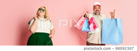 Portrait of stylish woman and smiling man with shopping bags, posing over pink studio background. Family weekend shopping 98092307