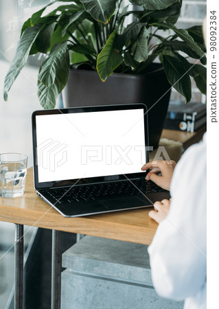 Online meeting. Office woman. Computer mockup. Unrecognizable lady working laptop with blank screen in light room interior. 98092384