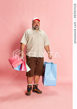 Portrait of mature man in casual clothes going shopping, posing with shopping trolley over pink studio background. Holiday shopping Portrait of mature man in casual clothes going shopping, posing with shopping trolley over pink studio background. Holiday shopping 98092426