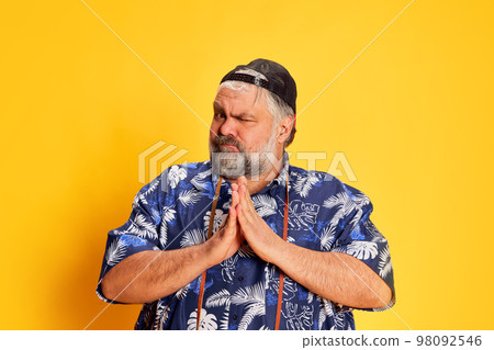 Portrait of fat mature man in stylish shirt posing with funny grimace face over bright yellow studio background Portrait of fat mature man in stylish shirt posing with funny grimace face over bright yellow studio background 98092546
