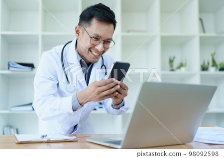Portrait of a doctor looking at a patient's information before treating a disease with using smart phone and computer in work. 98092598