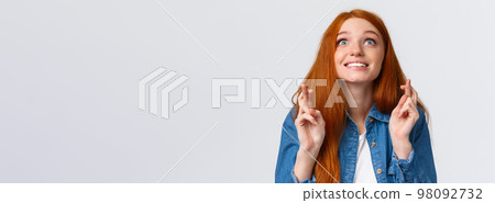 Excited and hopeful, optimistic cute redhead girl want dream come true, desire something, aspire achieve success good results, smiling looking up sky and making wish with fingers crossed good luck 98092732