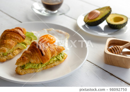 Croissant sandwich with egg,avocado on white dish and honey, coffee. breakfast and healthy food concept. Croissant sandwich with egg,avocado on white dish and honey, coffee. breakfast and healthy food concept. 98092750