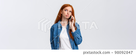Perplexed over decisions. Unsure cute redhead woman order take-away in favorite restaurant, calling someone on phone, look thoughtful, thinking, pondering answer while talking, holding smartphone 98092847