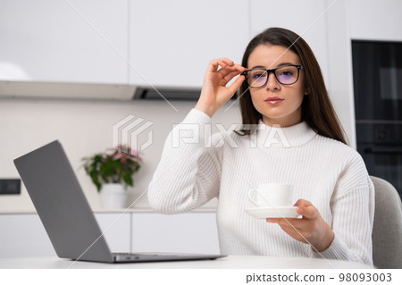Young businesswoman adjusting her glasses and holding a cup of coffee, working at the home office. Young businesswoman adjusting her glasses and holding a cup of coffee, working at the home office. 98093003