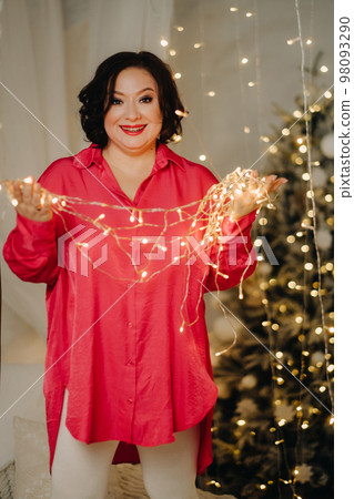 A woman in a red shirt in a room decorated for Christmas. Home New Year's atmosphere 98093290