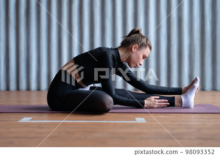 Woman leans forward stretches her back and legs. 98093352