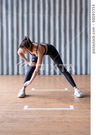 Woman exercising standing forward bend stretches of legs and lower back. 98093354