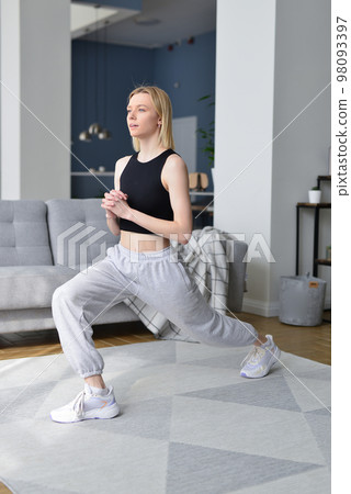 Woman performs lunges at home. 98093397