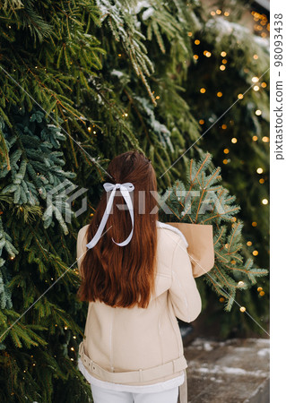A girl with long hair stands with her back in a winter forest with a bouquet of fir branches. Snowy winter A girl with long hair stands with her back in a winter forest with a bouquet of fir branches. Snowy winter 98093438