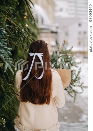 A girl with long hair stands with her back in the city with a bouquet of fir branches. Snowy winter A girl with long hair stands with her back in the city with a bouquet of fir branches. Snowy winter 98093440