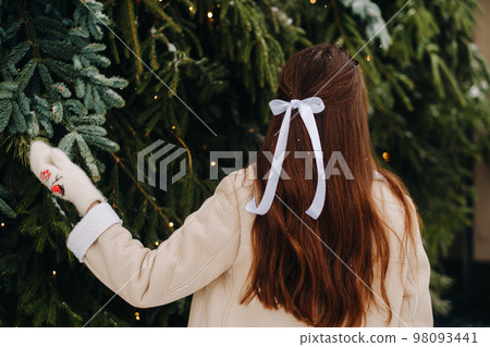 A girl with long hair stands with her back in a winter forest with a bouquet of fir branches. Snowy winter A girl with long hair stands with her back in a winter forest with a bouquet of fir branches. Snowy winter 98093441