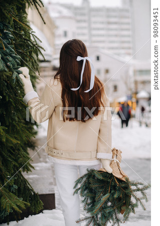A girl with long hair stands with her back in the city with a bouquet of fir branches. Snowy winter 98093451