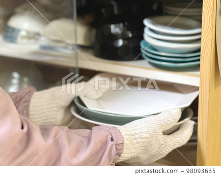 A hand with work gloves taking out a plate from the cupboard 98093635
