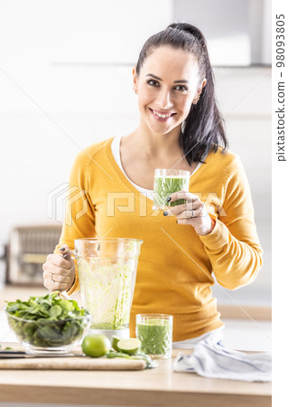 Smiling woman holding a glass of spinach green smoothie. Smiling woman holding a glass of spinach green smoothie. 98093805
