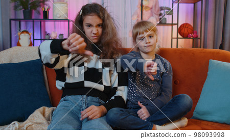 Upset siblings girls showing thumbs down dislike bad work disapproval, dissatisfied feedback at home Upset siblings girls showing thumbs down dislike bad work disapproval, dissatisfied feedback at home 98093998