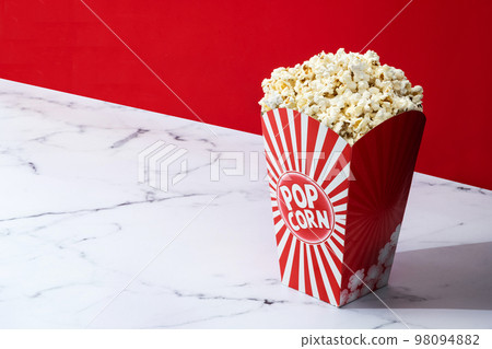 Salted popcorn in carton package on white marble and red background. Copy space Salted popcorn in carton package on white marble and red background. Copy space 98094882