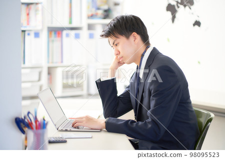 A young business person thinking while looking at a PC screen in the office 98095523