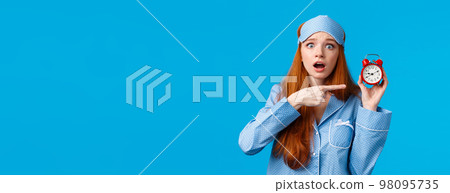 Shocked and concerned, worried cute redhead girl pointing at alarm clock with frustrated, nervous expression, being late, dont know how set up right time, standing blue background in nightwear Shocked and concerned, worried cute redhead girl pointing at alarm clock with frustrated, nervous expression, being late, dont know how set up right time, standing blue background in nightwear 98095735