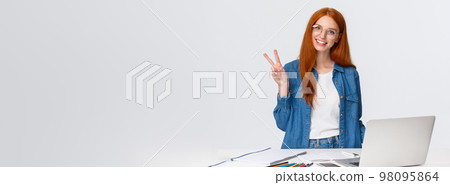 Lovely creative, good-looking redhead teenage girl likes draw, take online course, design something interesting, standing near table with laptop, colored pencils and paper, showing peace sign smiling 98095864