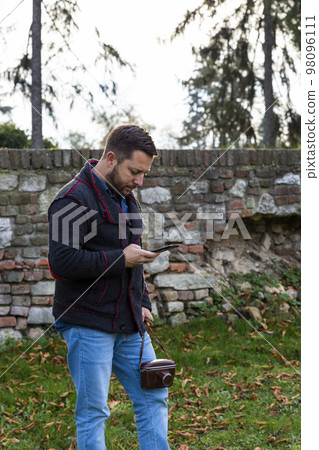 Photographer with vintage analogue film camera and smartphone outdoors Photographer with vintage analogue film camera and smartphone outdoors 98096111