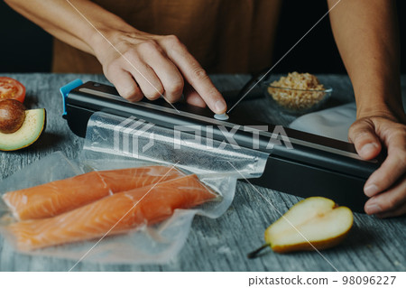 man vacuum-packs salmon in a vacuum bag 98096227