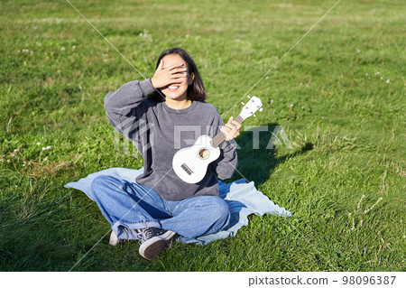 Excited asian girl sits in park with ukulele, plays instrument and feels happy upbeat, positive moments and people concept 98096387