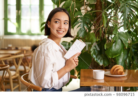 Tender, beautiful asian girl sitting with a book in cafe, reading and drinking coffee. People and lifestyle concept 98096715