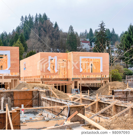 Wooden frame of new house with concrete filled fundation in front Wooden frame of new house with concrete filled fundation in front 98097093