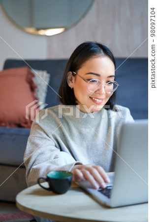 Young asian girl, freelancer professional sitting in living room and working with computer, studying at home using computer 98097104
