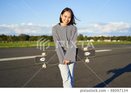 Portrait of beautiful asian girl skating on longboard, crusing with skateboard on empty road, enjoying freetime on fresh air Portrait of beautiful asian girl skating on longboard, crusing with skateboard on empty road, enjoying freetime on fresh air 98097134