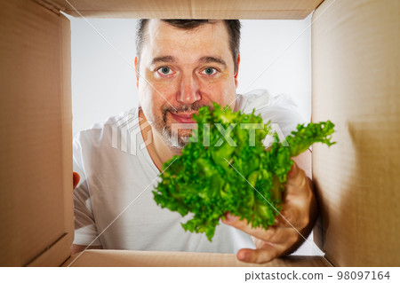 Happy man unpacking, opening carton box and looking inside. Man smiling unpacking and carton box 98097164