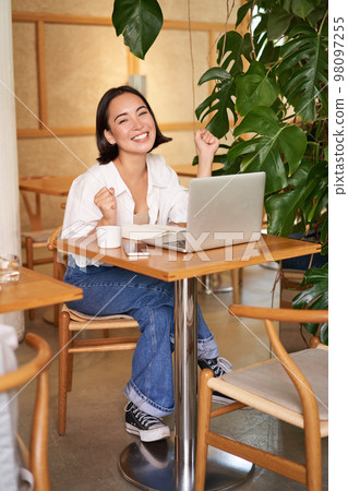 Happy young asian woman winning on laptop, receive good news, achieve goal at work, triumphing and smiling pleased, sitting in cafe Happy young asian woman winning on laptop, receive good news, achieve goal at work, triumphing and smiling pleased, sitting in cafe 98097255