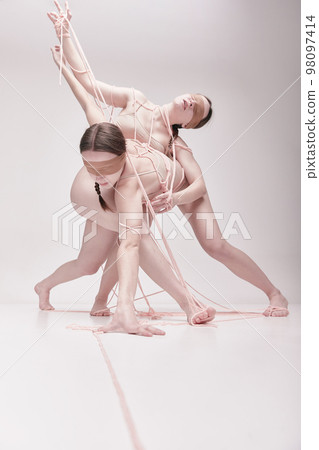 Manipulator. Portrait of two young girls posing in underwear and ropes with eyes closed over light studio background. Concept of weird people, contemporary photography 98097414