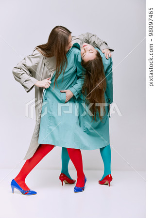 Portrait of two young girls in bright red, blue tights and coat posing over grey studio background. Vivid style, queer, art, fashion Portrait of two young girls in bright red, blue tights and coat posing over grey studio background. Vivid style, queer, art, fashion 98097465
