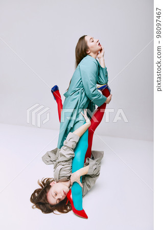 Portrait of two young girls in bright red and blue tights and coat posing over grey studio background. Self-expression. Vivid style, queer, art, fashion Portrait of two young girls in bright red and blue tights and coat posing over grey studio background. Self-expression. Vivid style, queer, art, fashion 98097467
