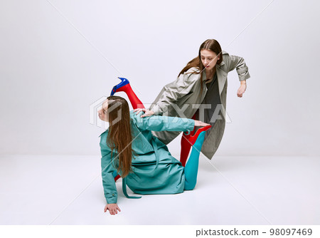 Portrait of two young girls in bright red and blue tights and coat posing over grey studio background. Friendship. Vivid style, queer, art, fashion Portrait of two young girls in bright red and blue tights and coat posing over grey studio background. Friendship. Vivid style, queer, art, fashion 98097469