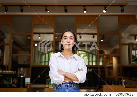 Smiling young female manager, cafe owner cross arms on chest, looking confident, standing in front of restaurant Smiling young female manager, cafe owner cross arms on chest, looking confident, standing in front of restaurant 98097632