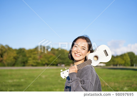 Young hipster girl, traveler holding her ukulele, playing outdoors in park and smiling 98097695