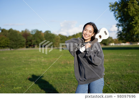 Beautiful korean girl posing with ukulele, young musician playing outdoors in green park on sunny day 98097696