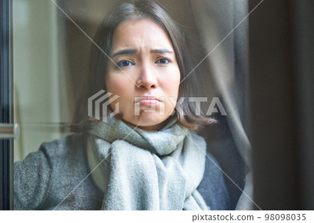 Portrait of sad ill woman staying at home, looking out of the window with jealous and upset face, cant leave home as being sick with covid-19 98098035