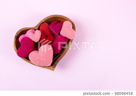 Multicolored pink knitted hearts in a wooden bowl in the shape of a heart on a pink background. Happy Valentine's Day, Mother's Day and birthday greeting card. 98098458