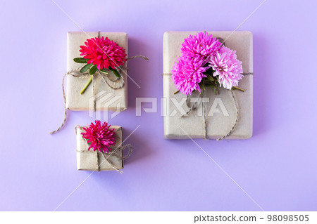 Gift box in gray craft paper decorated with vinous aster flowers on a purple background for the holiday Gift box in gray craft paper decorated with vinous aster flowers on a purple background for the holiday 98098505