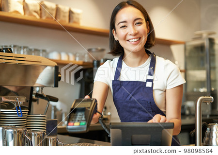 Small business and people. Smiling asian woman barista, working in cafe, giving POS terminal, credit card machine, processing order 98098584