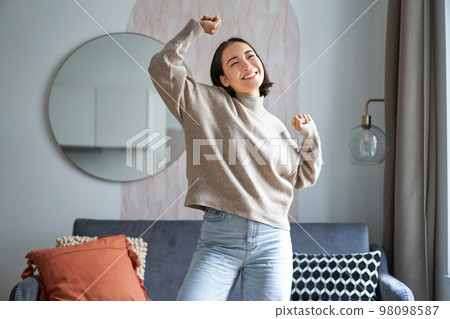 Portrait of happy asian woman dancing, rejoicing and triumphing, feeling upbeat at home 98098587