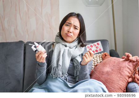 Korean woman showing medical pills, sore throat sprays, feeling sick, staying at home as feeling unwell, catching cold in winter Korean woman showing medical pills, sore throat sprays, feeling sick, staying at home as feeling unwell, catching cold in winter 98098696